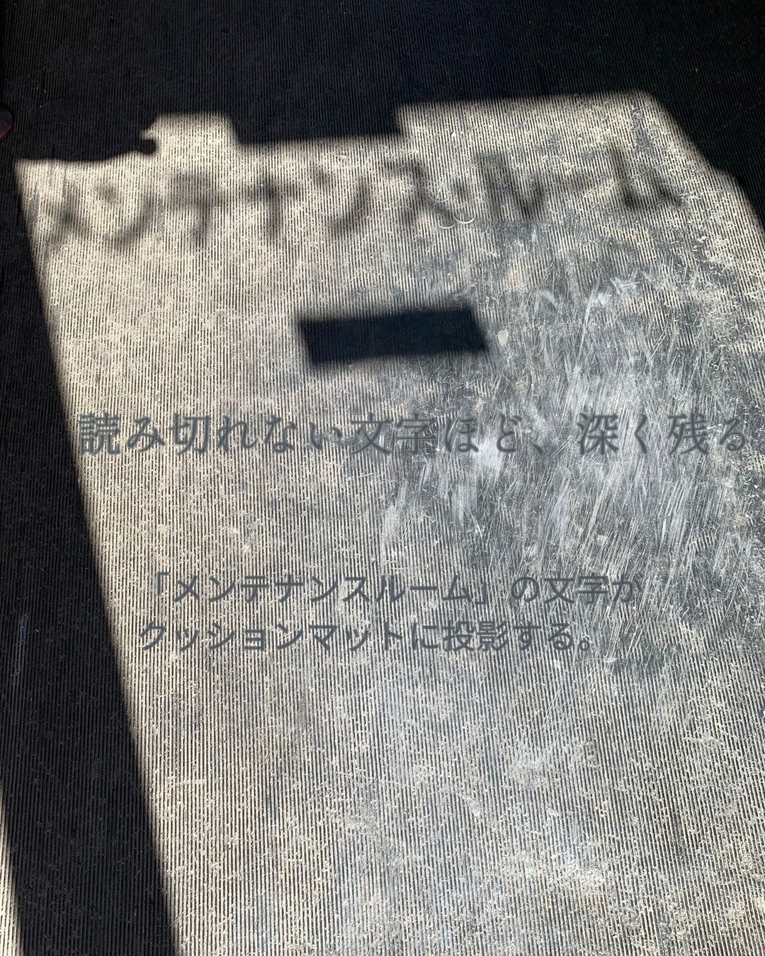 「メンテナンスルーム」の文字の影が地面に落ち、西日で読めそうで読めない抽象的な形になっている写真。