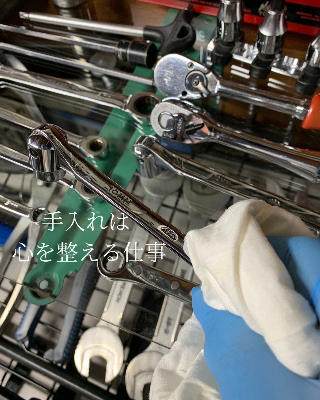 閉店後の整備室で、手袋をした手が工具を一つずつ拭き上げて手入れしている様子。