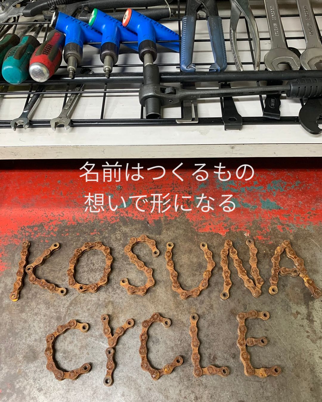 錆びた自転車チェーンを組み合わせて作られた「KOSUNA CYCLE」の文字。赤い作業台の上に置かれた手作りのロゴ。