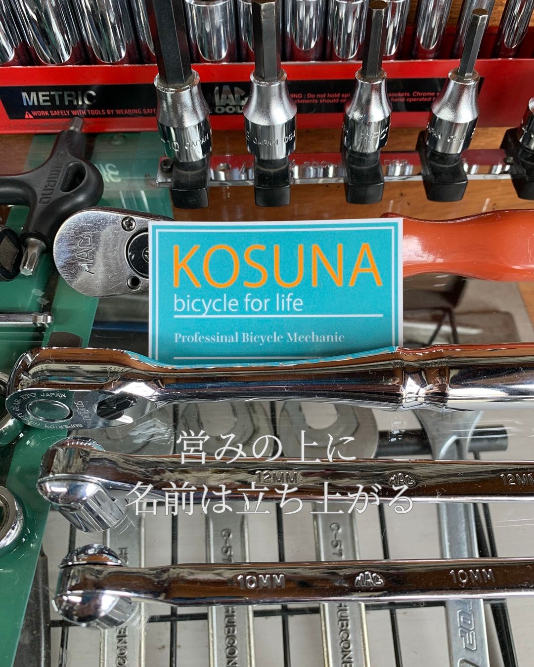 工具が並ぶ作業台の上に置かれたKOSUNAのグリーンロゴステッカー。日々の整備作業と店の誇りが重なり合う瞬間。