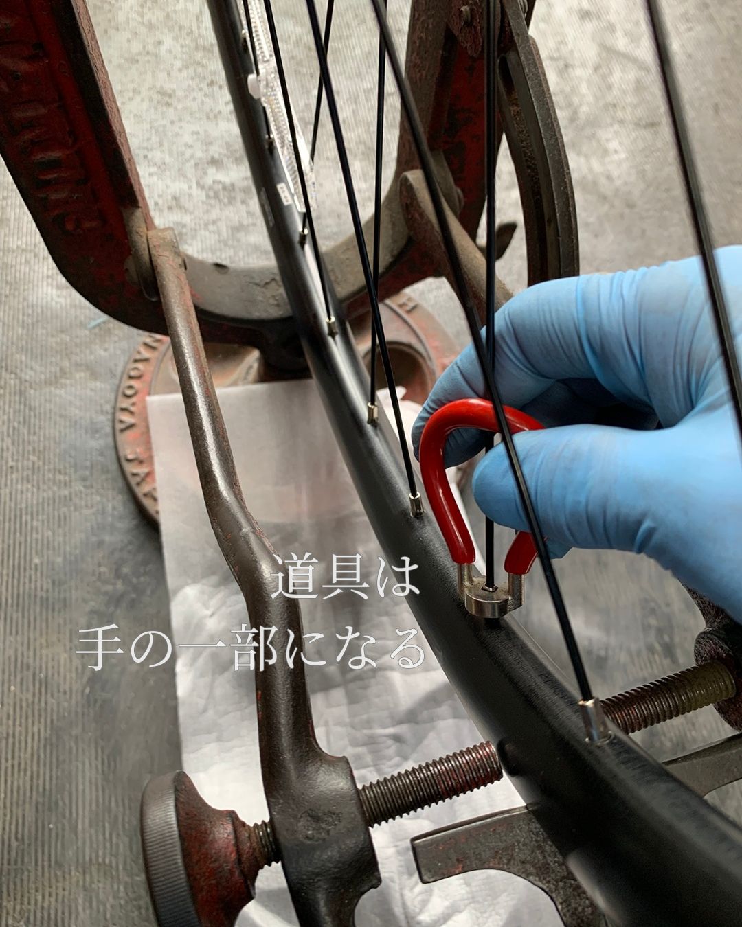 自転車ホイールの振れを調整する作業中の手元。使い込まれた工具が手の延長のように扱われている様子。